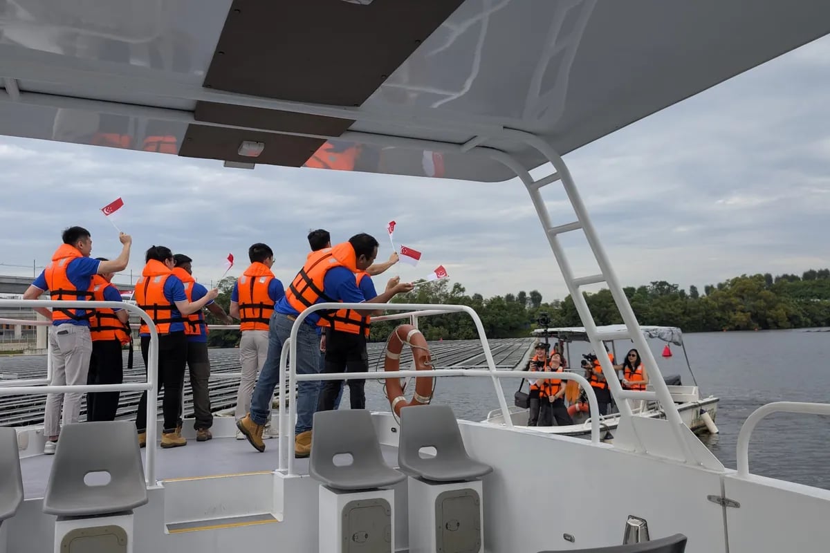 Filming on a boat at the floating solar farm as people in orange life vests wave Singapore flags.
