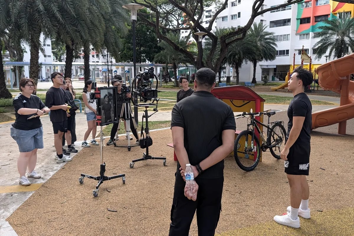 A film crew setting up a shot at an HDB playground, cameras and monitors on stands under the trees.